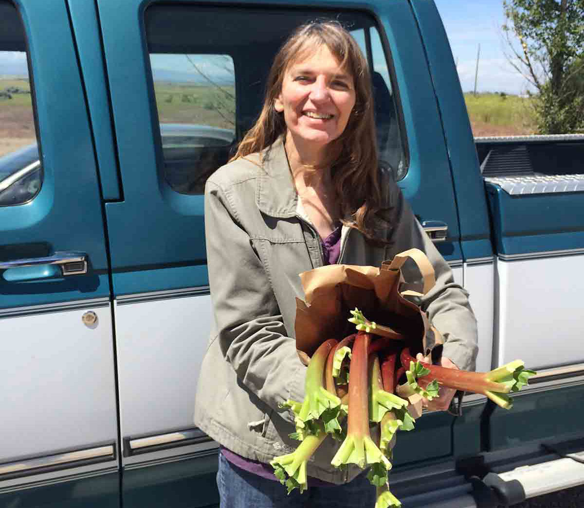 Cathy standing in front of pickup holding a bag rhubarb.