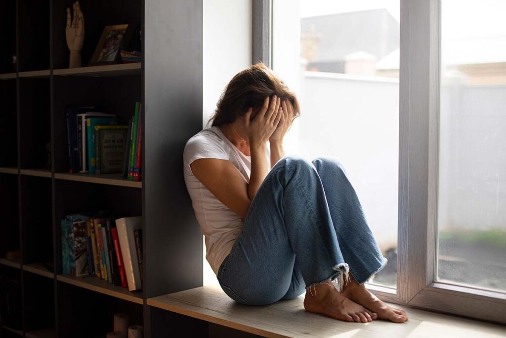 Discouraged young woman sitting by window at home,