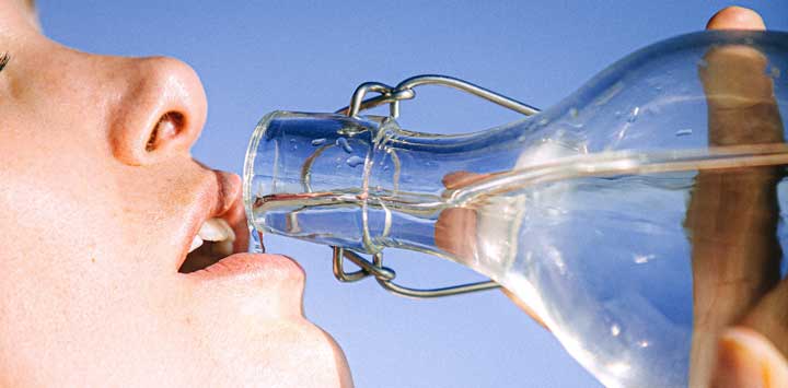 Woman drinking water from a glass bottle.