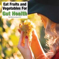 Woman wearing a hat looking at grapes with overlay: Eat Fruits and Vegetables for Gut Health