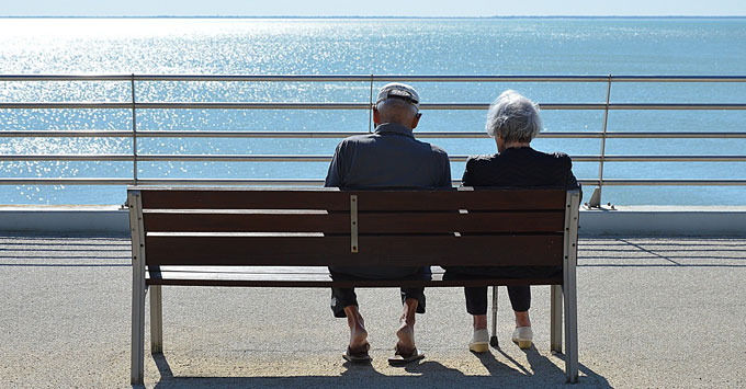 Elderly couple sitting on a bench looking at the ocean.