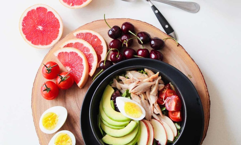 Bowl of chicken, tomatoes, apple slices, and avocado slices. With grapefruit, cherries, and hardboiled eggs.