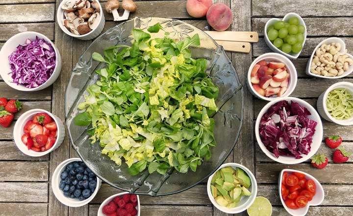 A large glass salad bowl with different fruits, veggies, and nuts on the side.