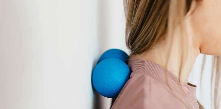 Woman massaging neck with two blue lacrosse balls.