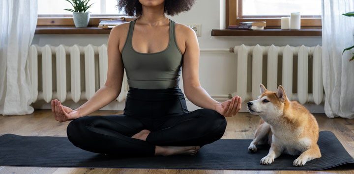 Woman meditating with dog next to her.