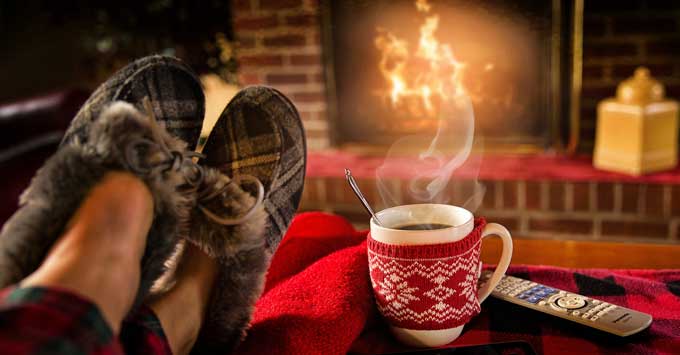 Feet in slippers with hot drink in mug in front of fireplace