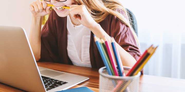 Woman biting and breaking a pencil while looking at a laptop.