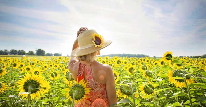 Woman wearing a big hat with sunflower on it in a field of sunflowers.