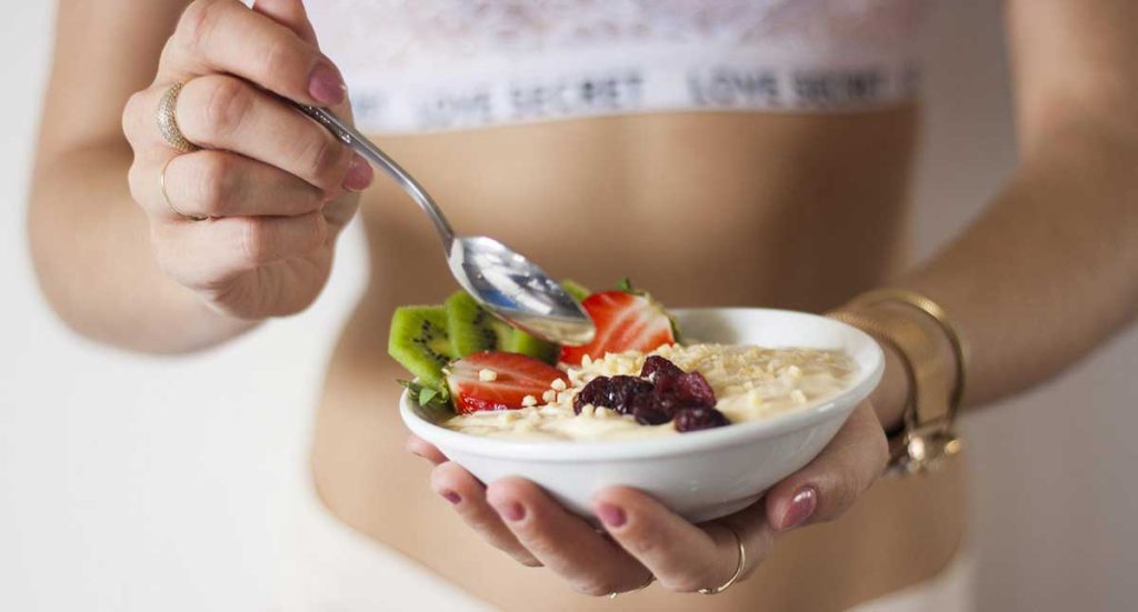 Young woman eating a healthy bowl of fruit and gluten-free oats.