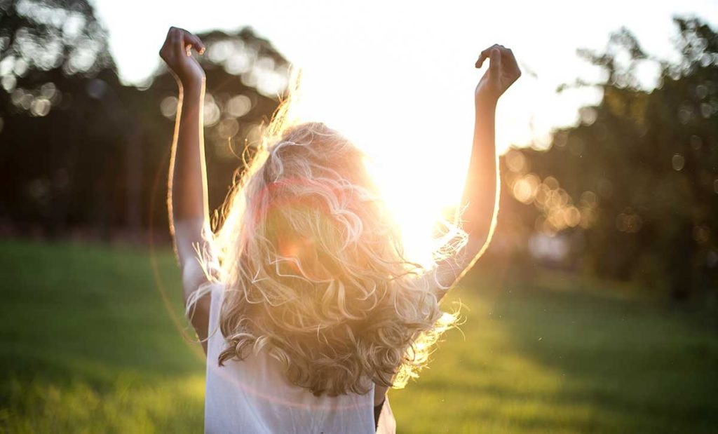 Young woman facing sun with arms in air.