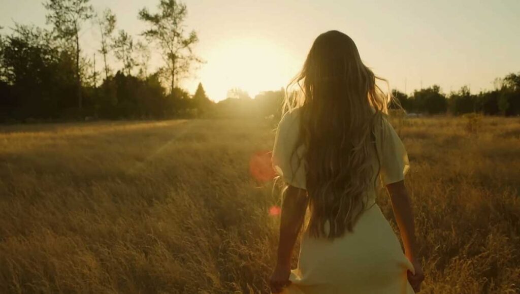 Woman with long blond hair in field looking towards sunset.