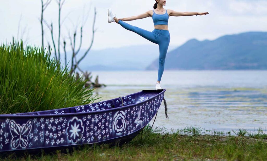 Woman in yoga pose standing on the edge of a canoe.