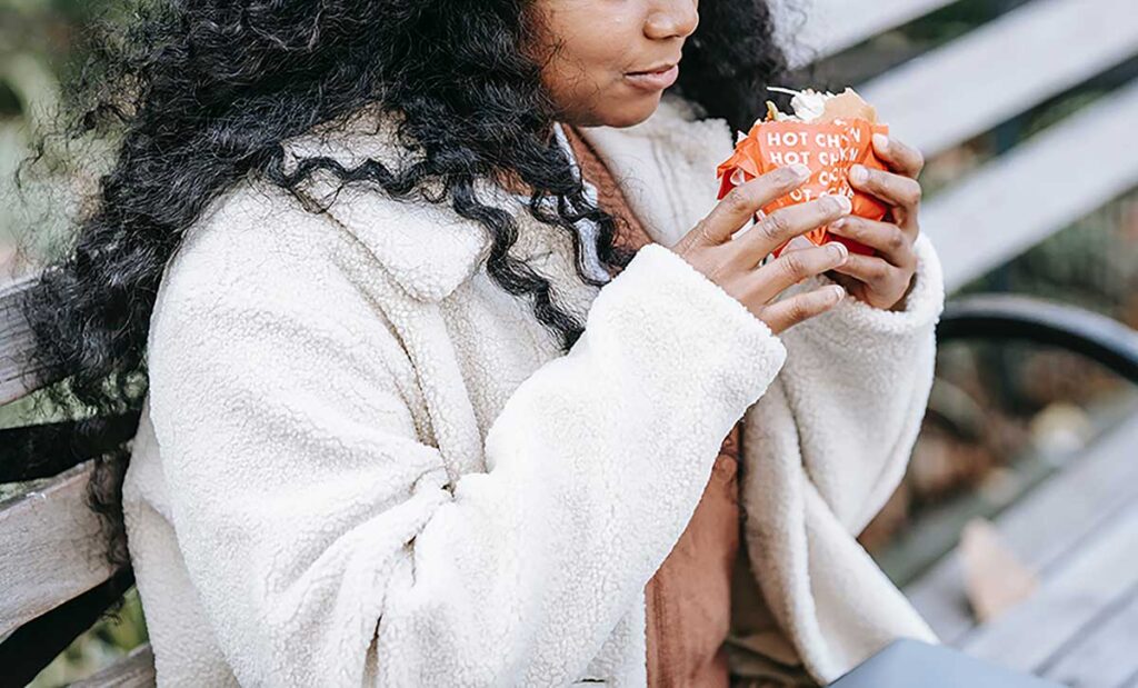 Woman on park bench eating a hamburger.
