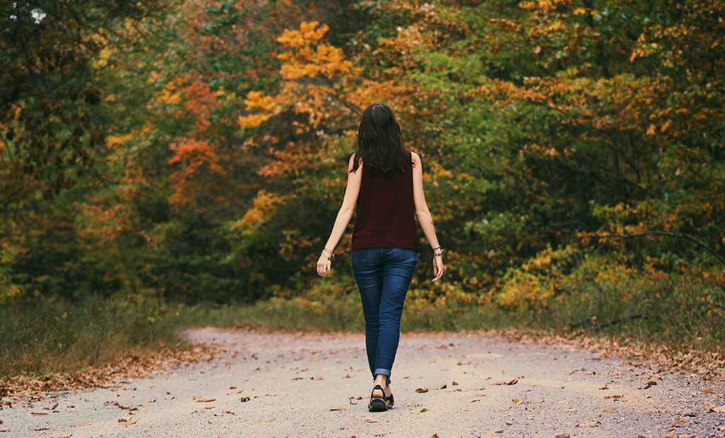 Woman walking away on path with fallen autumn leaves.