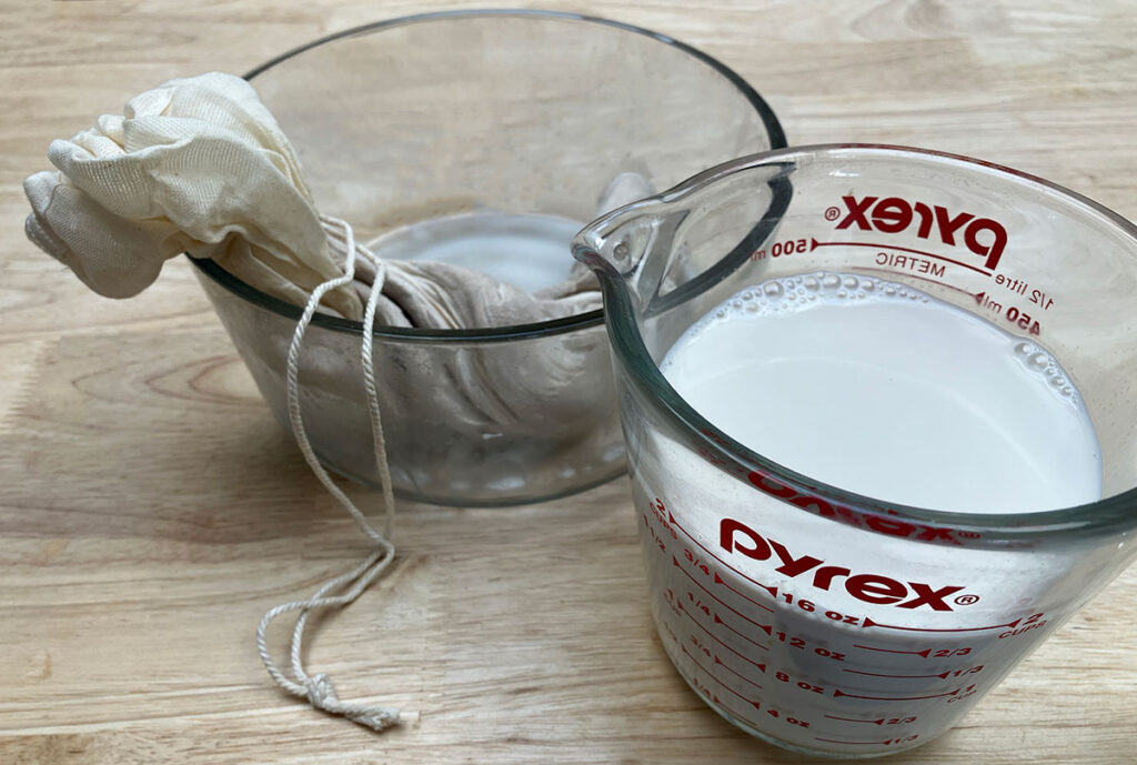 Almond milk in Pyrex measuring cup and nug bag in glass bowl.