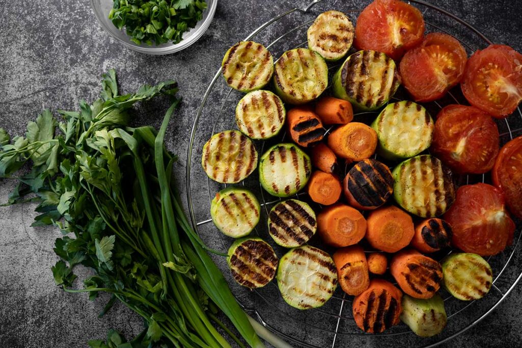 Assortment of grilled vegetables with herbs on dark background.