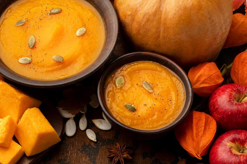 Pumpkin soup topped with pumpkin seeds and apples on the side.