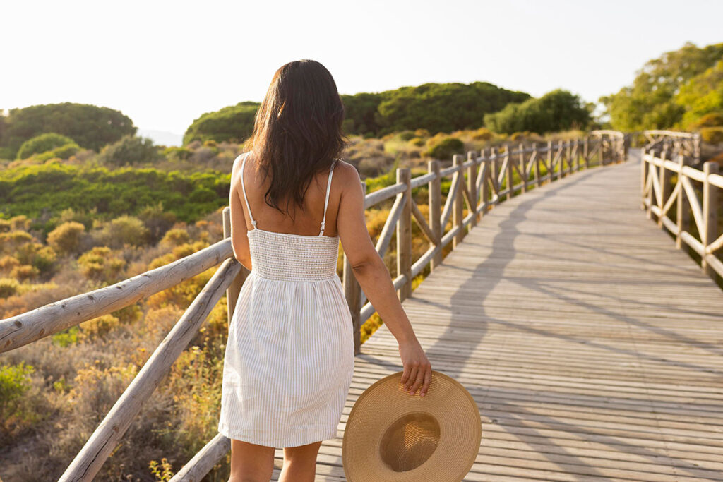 Back view of women holding a hat on wooden trail.