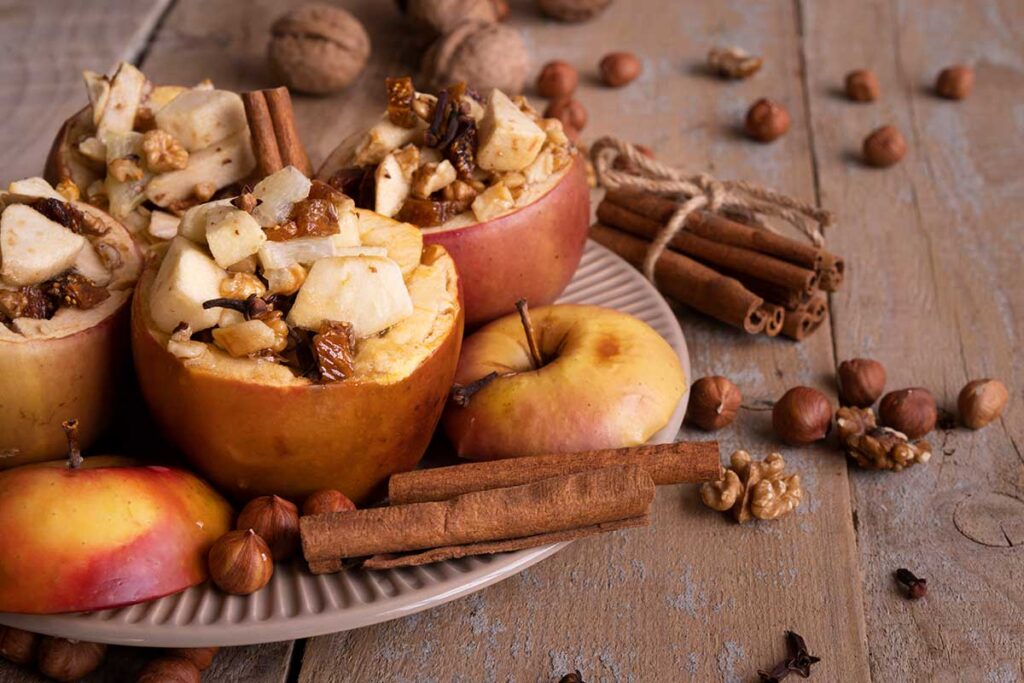 Baked apples on plate with nuts and cinnamon sticks on wooden background.