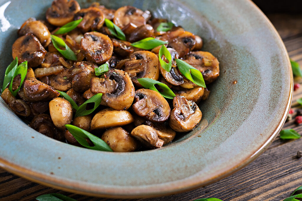 Baked mushrooms with herbs in a ceramic bowl on wooden table.