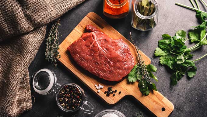 Beef steak on cutting board with seasonings and herbs.