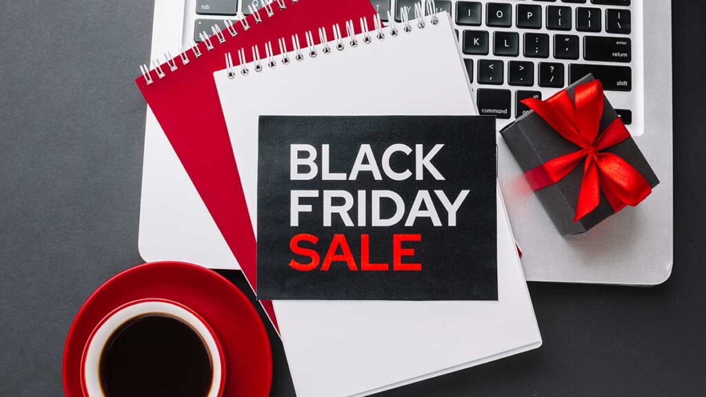 Black Friday Sale sign with top of red and white notebooks and small Christmas gift on a laptop.