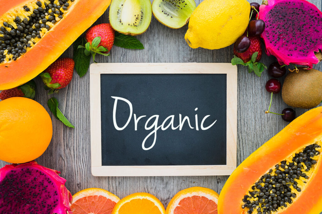 Blank blackboard with Organic written on it surrounded by summer fruits.