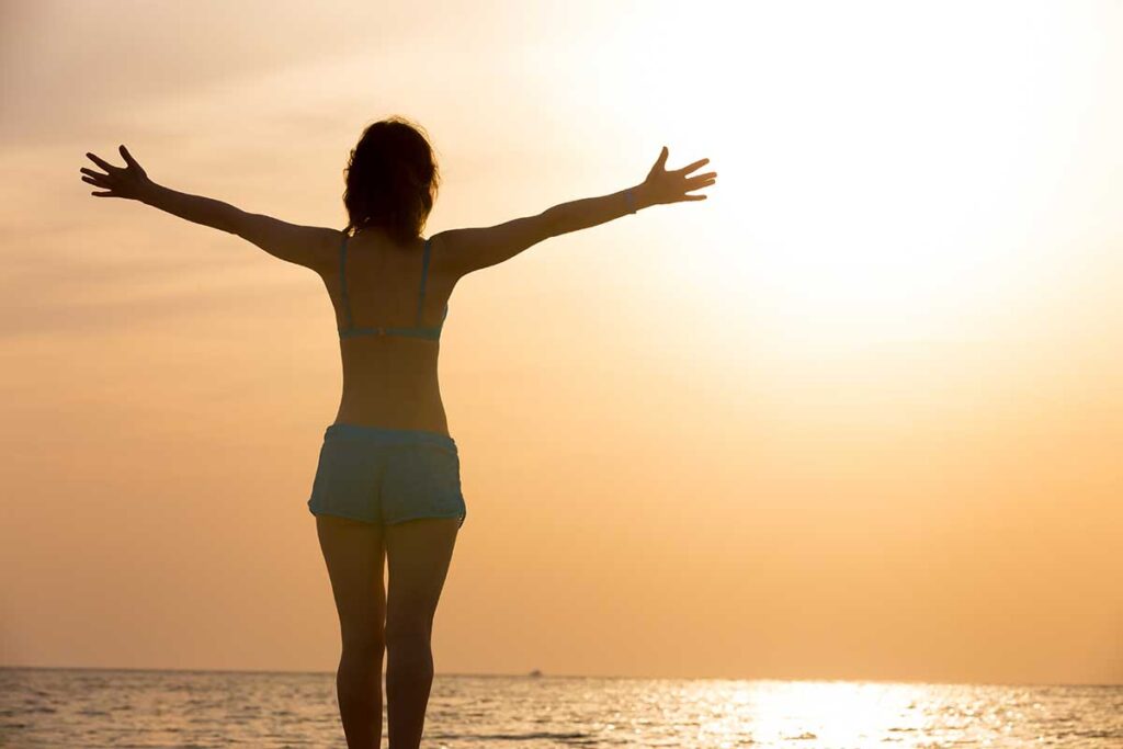 Bliss, woman with open arms looking into the sunset over the ocean.