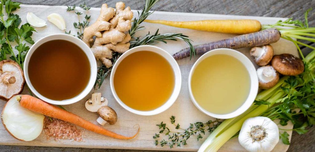 Three broths in bowls on cutting boards with veggies.