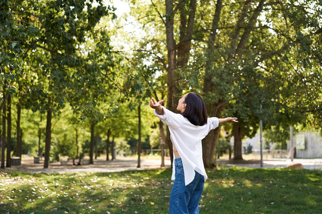 Carefree young woman dancing enjoying the sun on summer day in the park.
