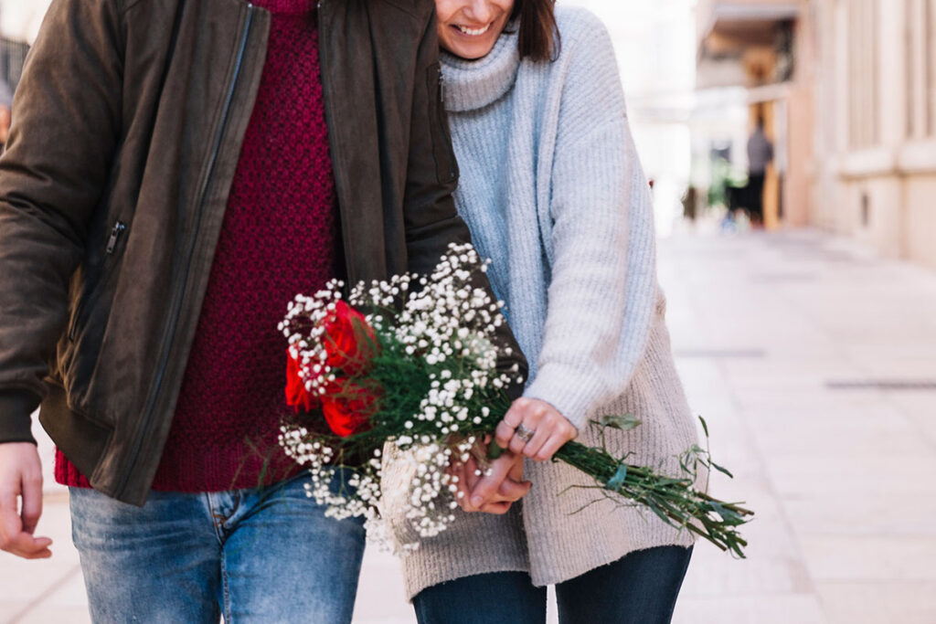 Cheerful couple with bouquet walking down street.