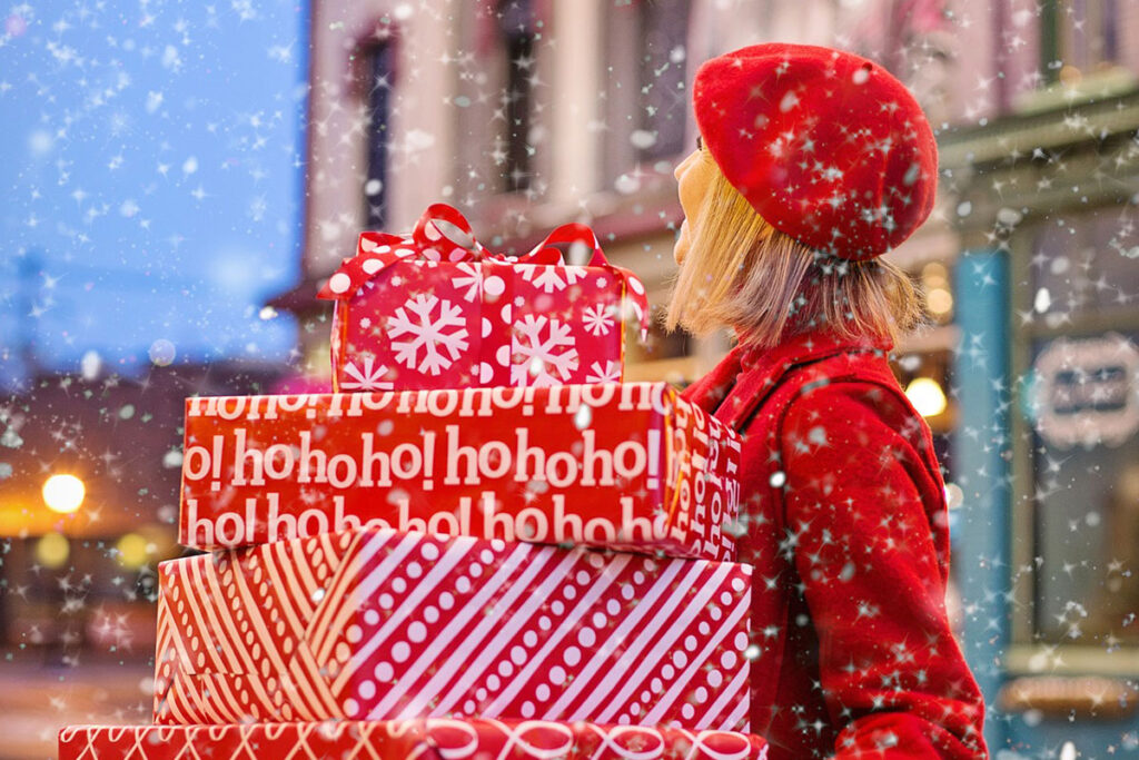 Woman in red holding Christmas presents while it's snowing.