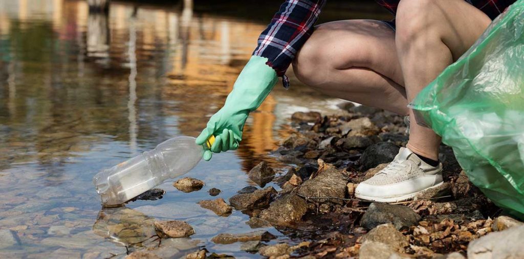 Woman picking up a plastic water bottle from the river.