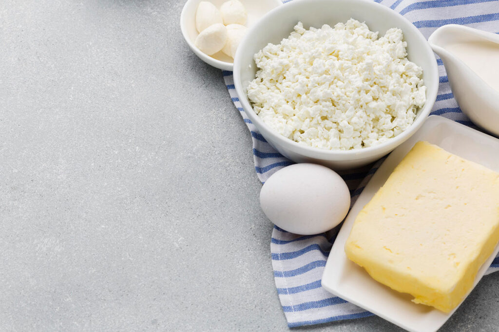 Close-up cottage cheese, egg, and butter on blue and white striped cloth.