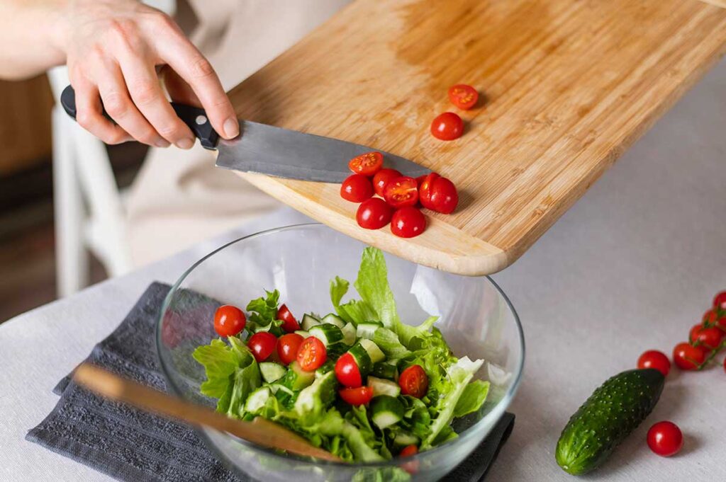 Close up of woman scraping tomatoes off cutting board into a salad.