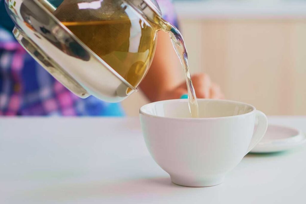 Close up of tea flowing from teapot into cup.