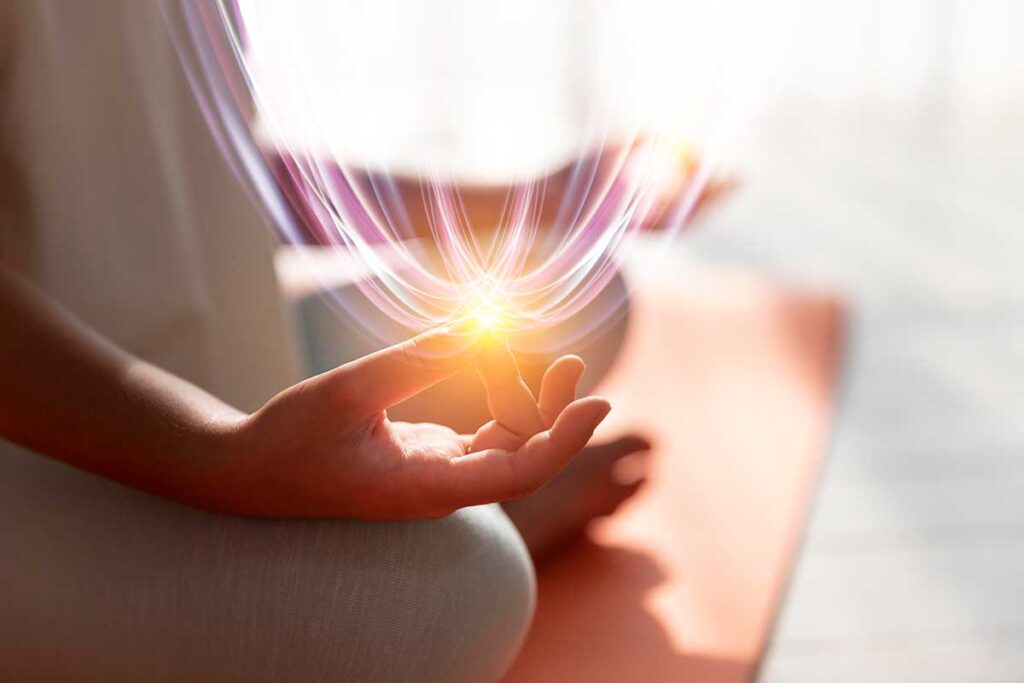 Close up of woman meditating with light illuminating from her fingertips.