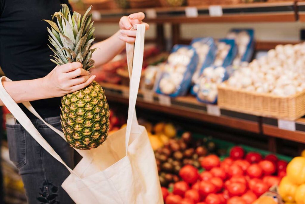 Close-up woman putting a pineapple in a bag.