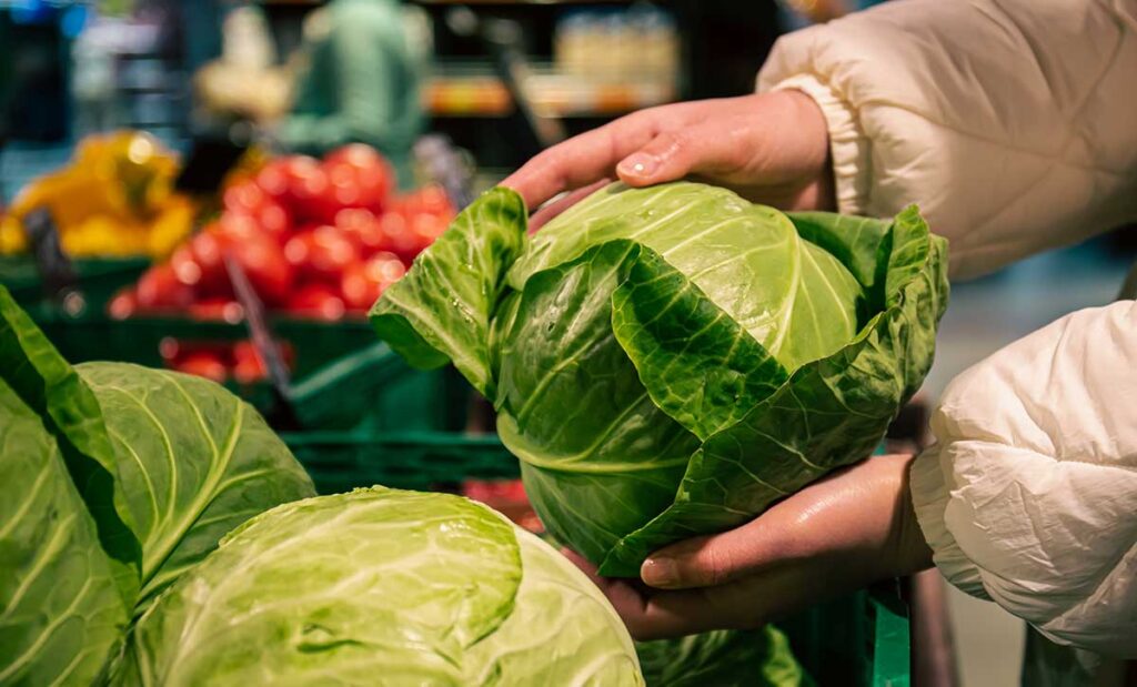 Closeup of woman holding cabbage in grocery store.