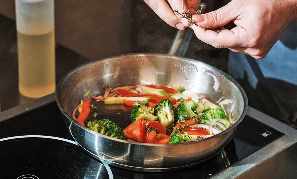 Adding herbs to veggies in skillet.