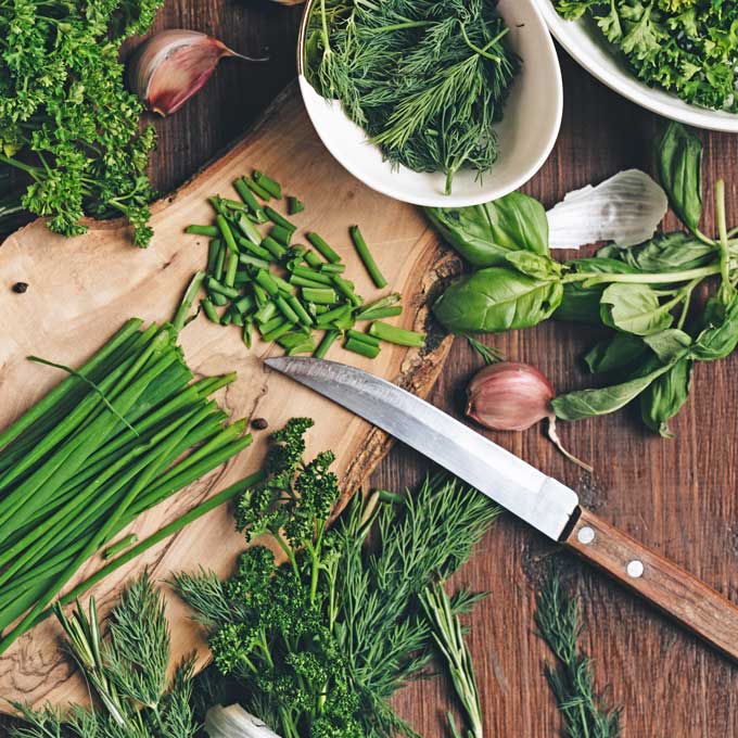 Different herbs on cutting board with knife.