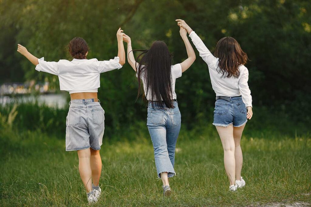 Friends walk walking away on grass holding hands together and up in the air.