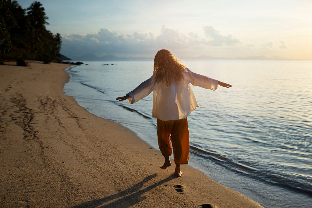 Full shot woman walking barefoot on beach.