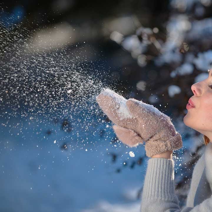 Young woman blowing snow from her mittens.