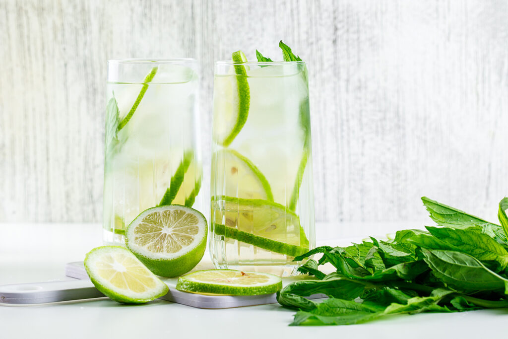 Glasses with lemon and basil on cutting board.