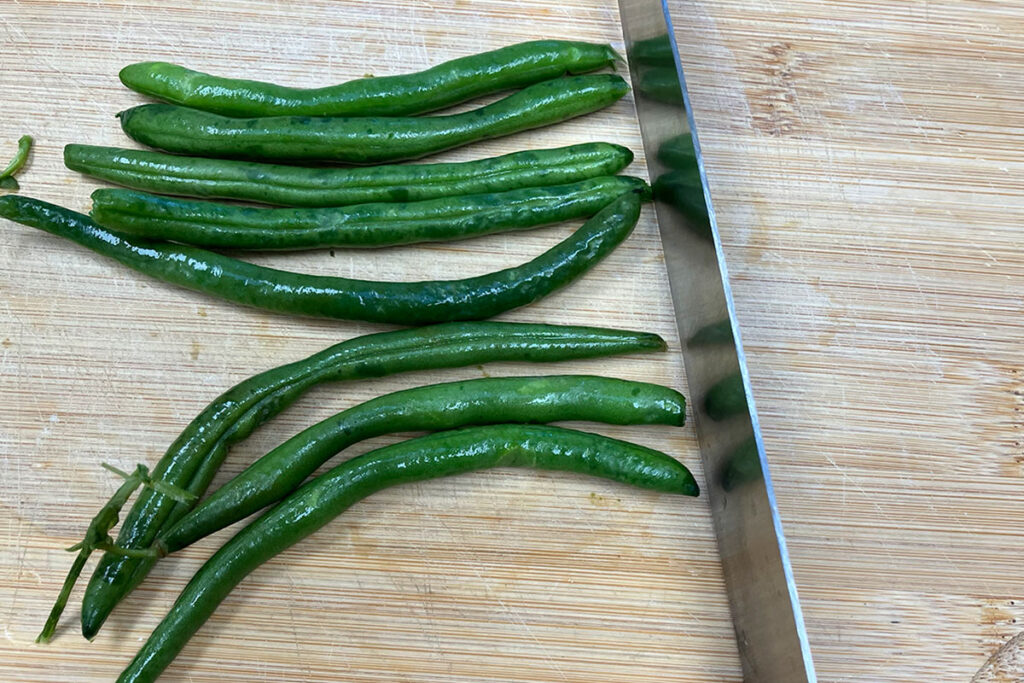 Green beans lined up on cutting board.