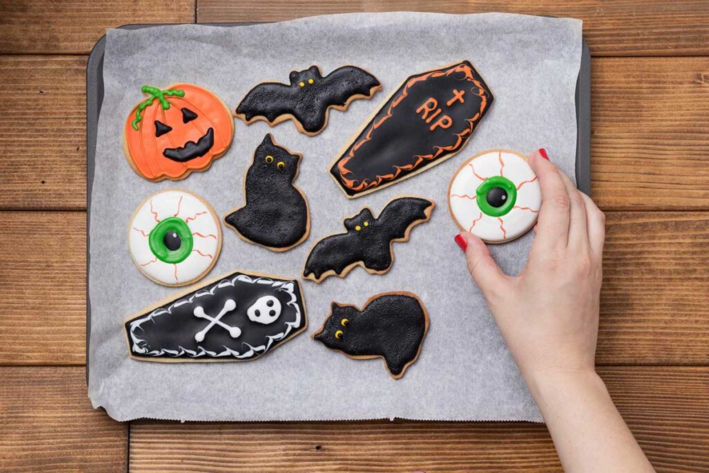 Woman holding a Halloween cookie on a baking sheet with other cookies.