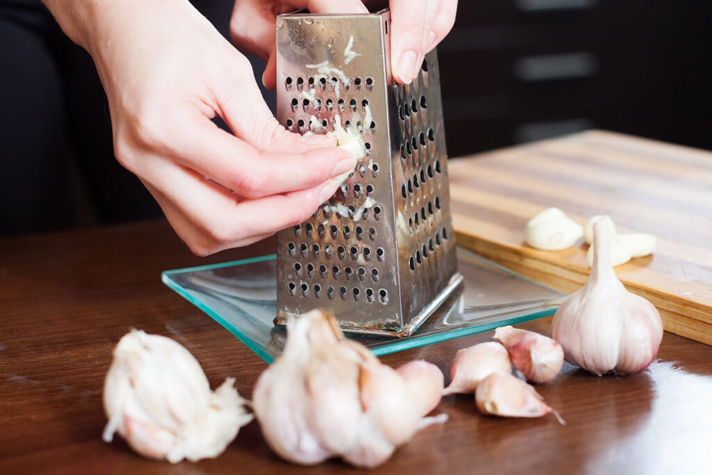 Female hands grating garlic on a grater.