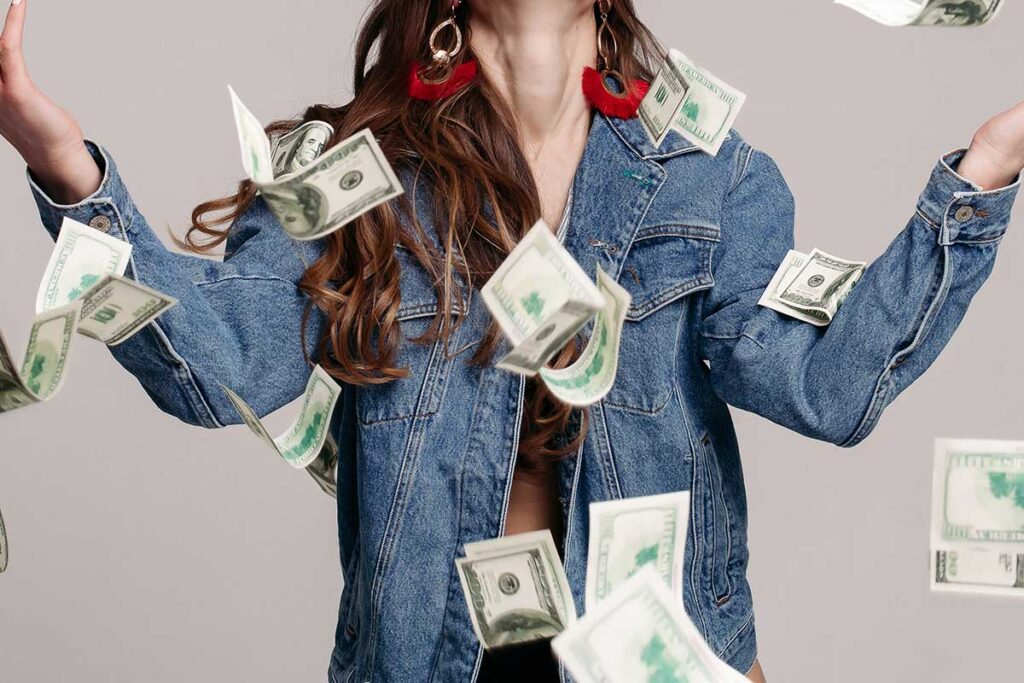 Happy laughing girl in denim jacket with flying dollar bills around.