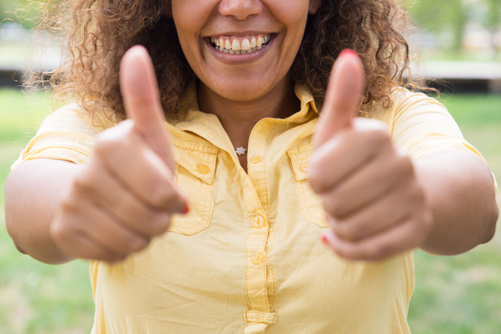 Happy woman showing thumbs up and posing at camera in park.